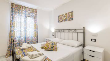 A bedroom with a bed, a nightstand, a wall-mounted light, and a window with curtains.