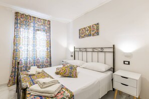 A bedroom with a bed, a nightstand, a wall-mounted light, and a window with curtains. - Apartment 'Stella Marina' with Shared Pool, Wi-Fi and Air Conditioning (Granelli)