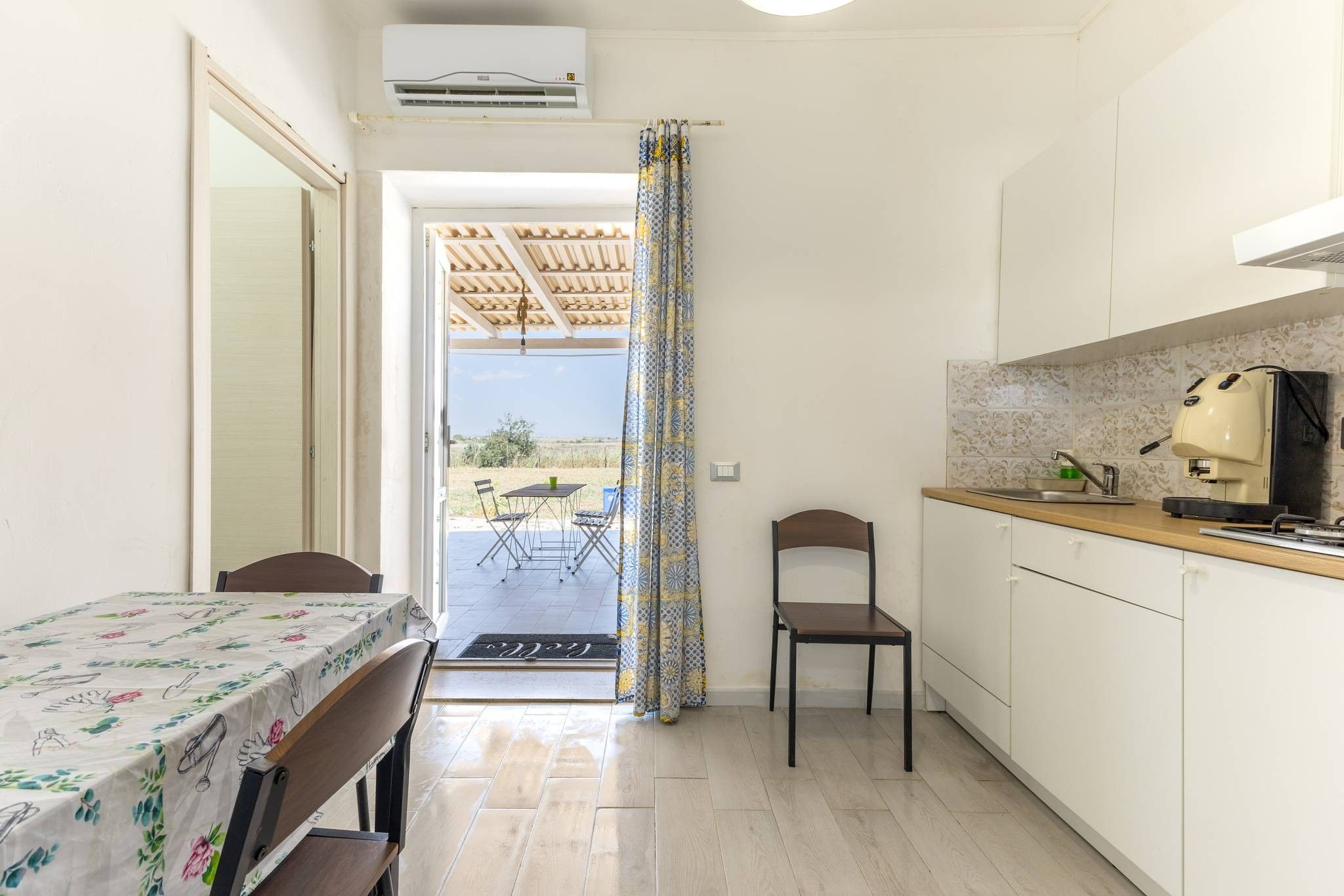 Una cucina compatta con angolo ristoro, una macchina per caffè e vista su un patio esterno attraverso una porta.