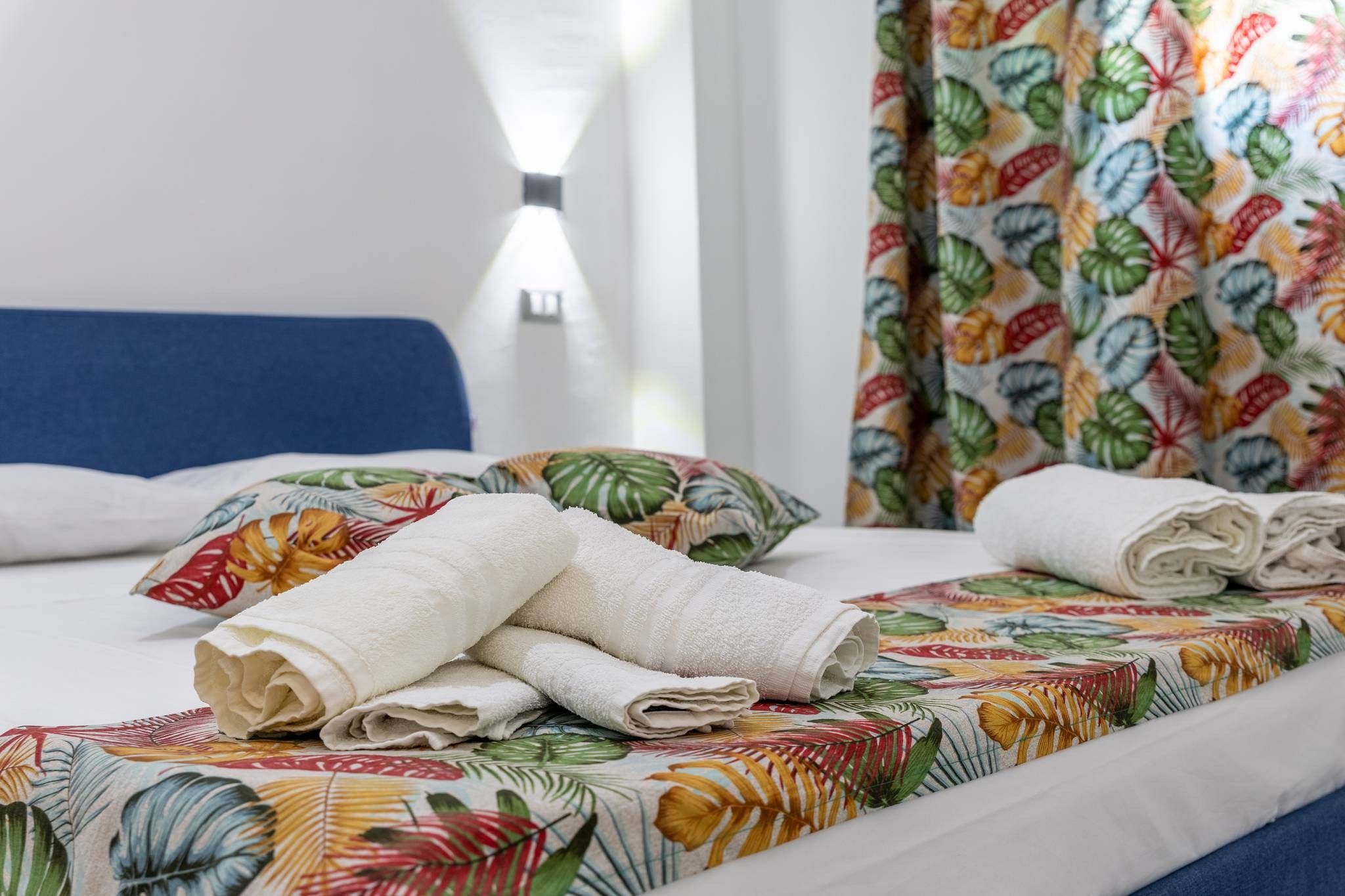 Una camera d'albergo con un letto, asciugamani bianchi e una coperta con motivi floreali.