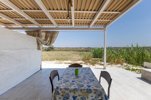 A covered outdoor dining area with a table and chairs, a view of a field, and a clear sky.