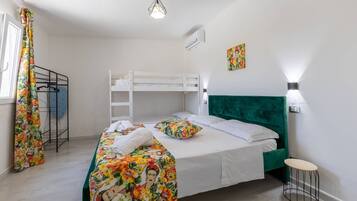 Une chambre avec un lit superposé, une tête de lit recouverte d’un tissu vert, une couvre-lit à motifs floraux et un petit tabouret.