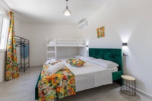 Un dormitorio con una cama litera, cabecera tapizada de color verde, colcha con estampado floral y un pequeño taburete.