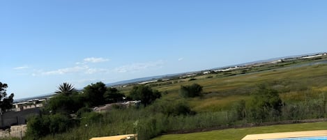 A swimming pool with a wooden deck, surrounded by a grassy lawn and a view of distant fields.