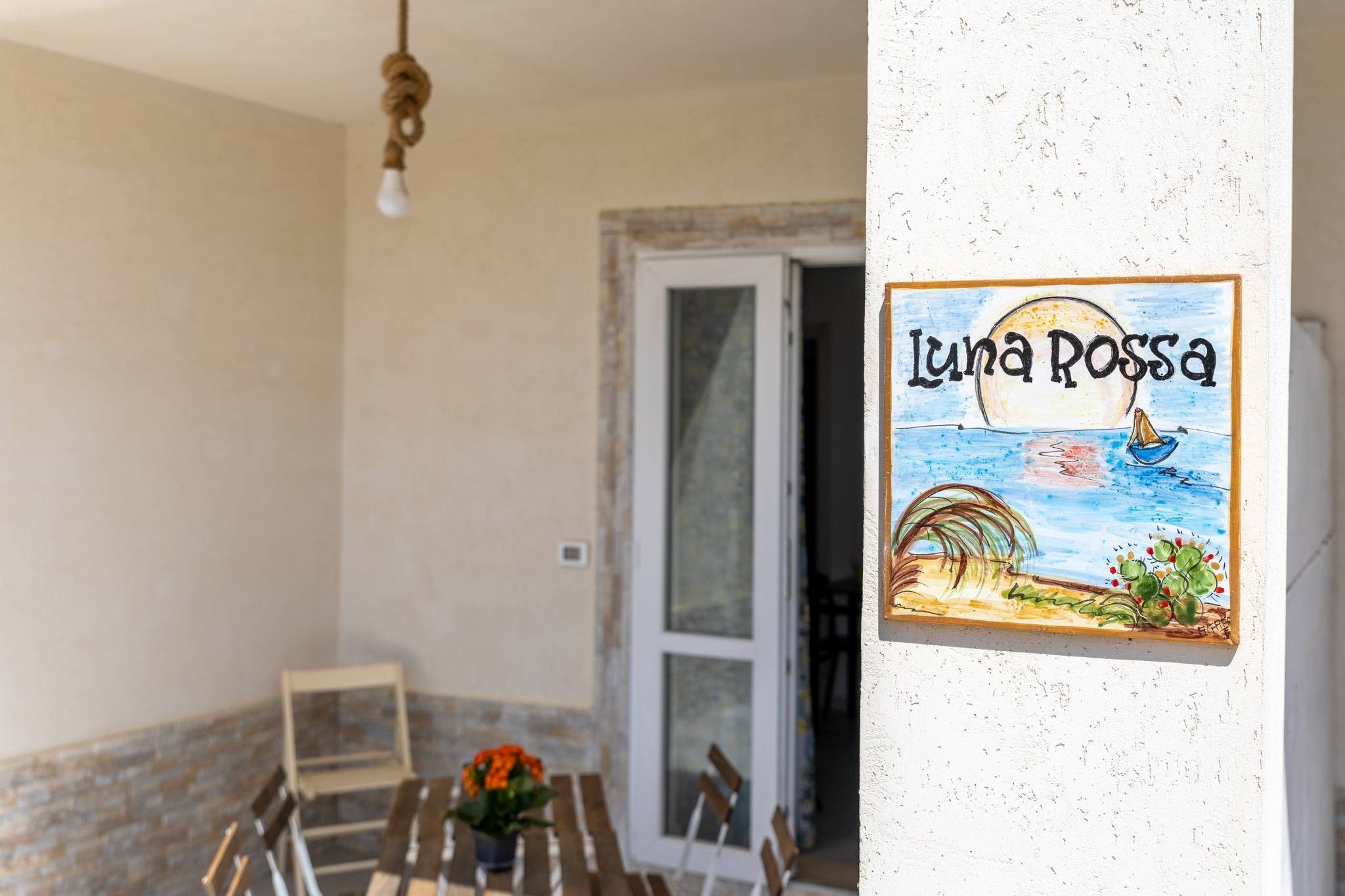 Una stanza con un tavolo, sedie, una pianta in vaso e un quadro appeso al muro intitolato 'Luna Rosa'.