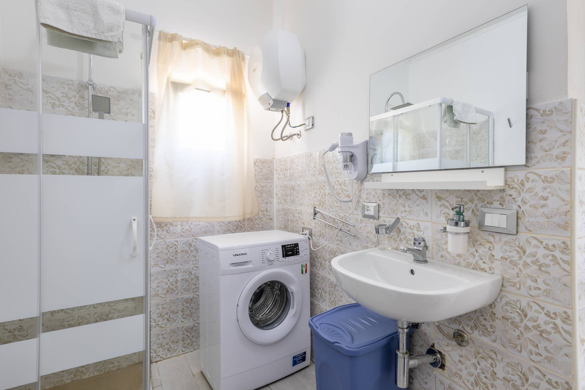 Ein kleines Badezimmer mit Waschmaschine, Waschbecken und Spiegel.