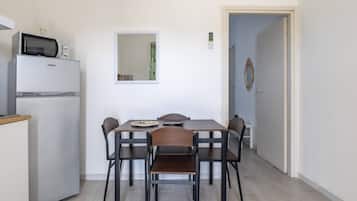 Una cucina compatta con frigorifero, microonde e un tavolo da pranzo con quattro sedie. Sopra il tavolo, è appeso uno specchio.