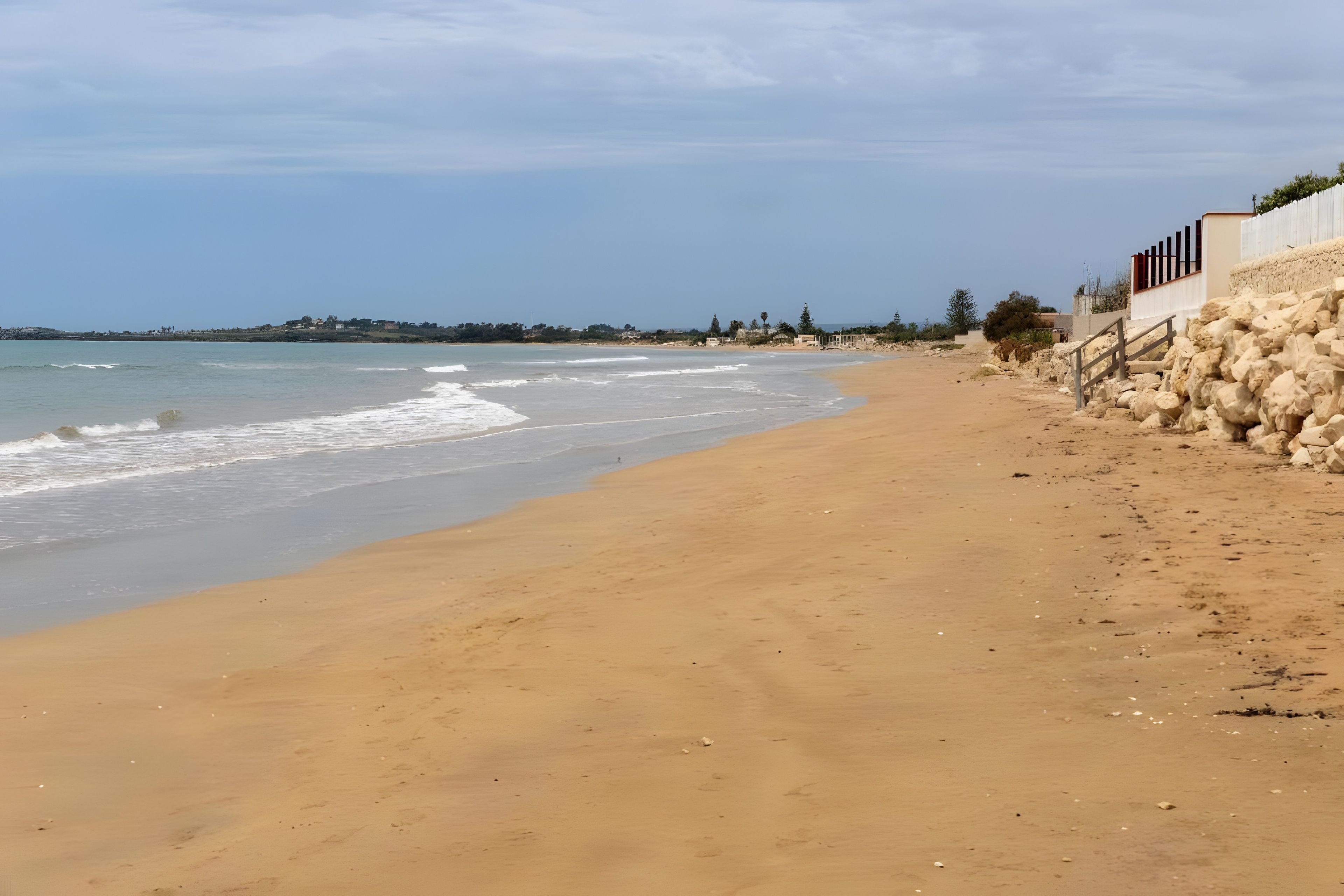 A sandy beach with a rocky wall and a clear sky.
