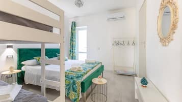 Una camera d'albergo con letti a castello, un letto con testiera verde, un tavolino rotondo, uno specchio e un appendiabiti.