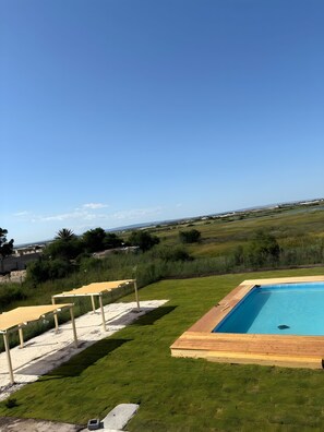 Una piscina con terraza de madera, rodeada de césped y vistas a campos lejanos.