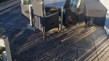 Eine Dachterrasse mit Tisch und Stühlen, Solaranlagen und Blick auf die Nachbarschaft.