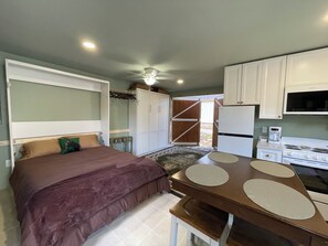 Ein kleines Schlafzimmer mit einem Einzelbett, einem kleinen Tisch und einer Küchenzeile inklusive Herd und Kühlschrank.