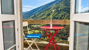 A balcony with a red table and blue chair, overlooking a mountainous landscape.