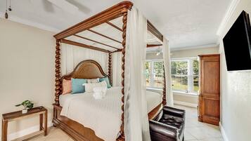 A four-poster bed with a canopy, a bedside table with a plant, and a view of the outdoors through a window.