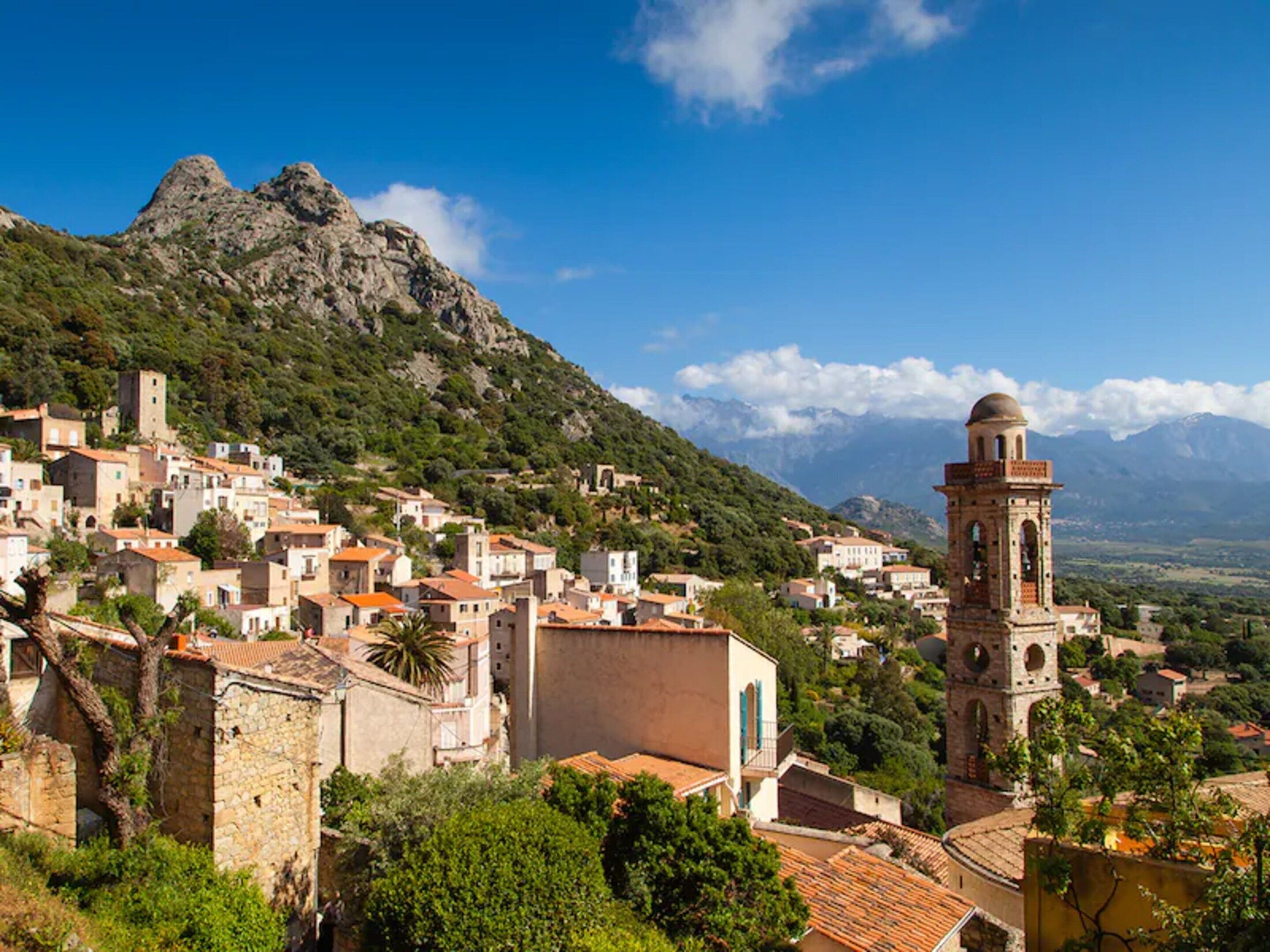 A coastal town with historic buildings, a prominent tower, and a mountainous backdrop.