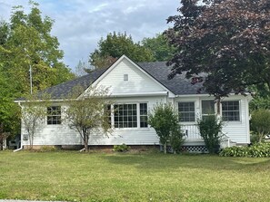 A single-story white house with a gabled roof, a front porch, and a small front yard. - A beach house home away from home with all the amenities (Fort Erie)