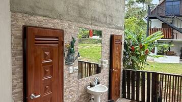 A stone-tiled patio with a white sink and two wooden doors, a small cactus, and a view of a house in the background.