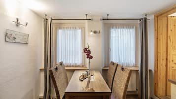 Zona pranzo con tavolo in legno, sedie in vimini e un vaso con fiori.