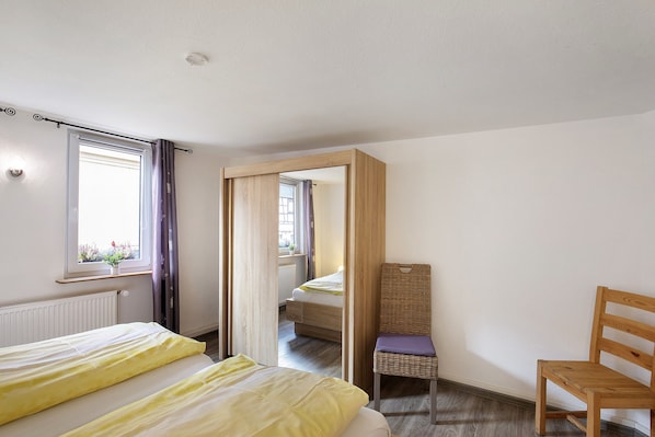 Un dormitorio con cama, una silla, un espejo y una ventana con cortinas.