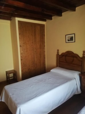 Een eenpersoonsbed met houten hoofdeinde in een kamer met een houten deur en een klein tafeltje.