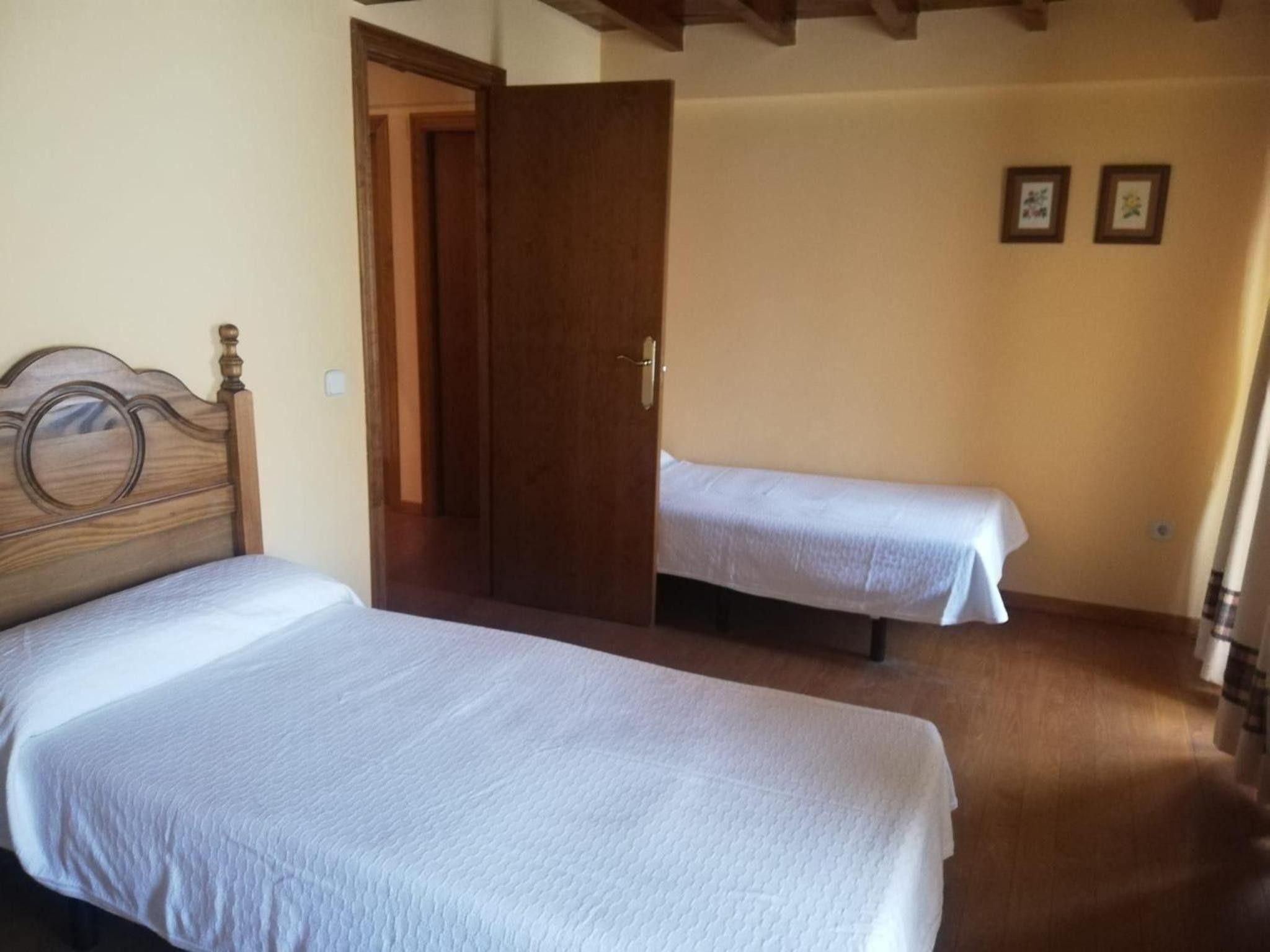 A room with two beds, wooden flooring, and a door leading to another room.