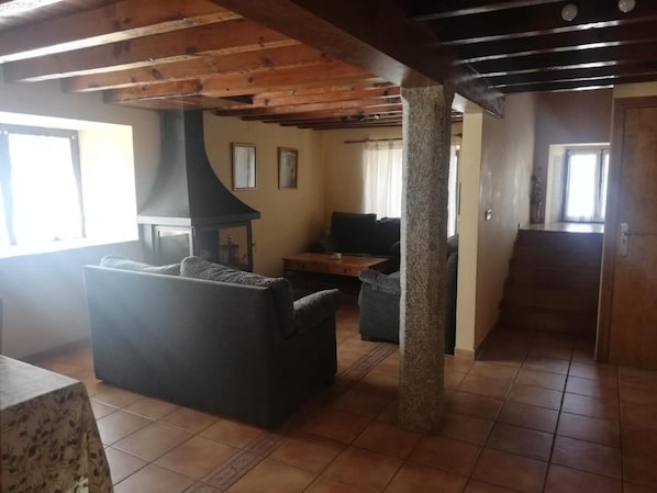 A living room with a fireplace, a sofa, a coffee table, and a stone pillar. - Country House 'Casa Rural Del Chopo' with Mountain View (La Aliseda de Tormes)