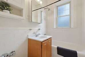 Un baño con lavamanos blanco, armario de madera y ventana.