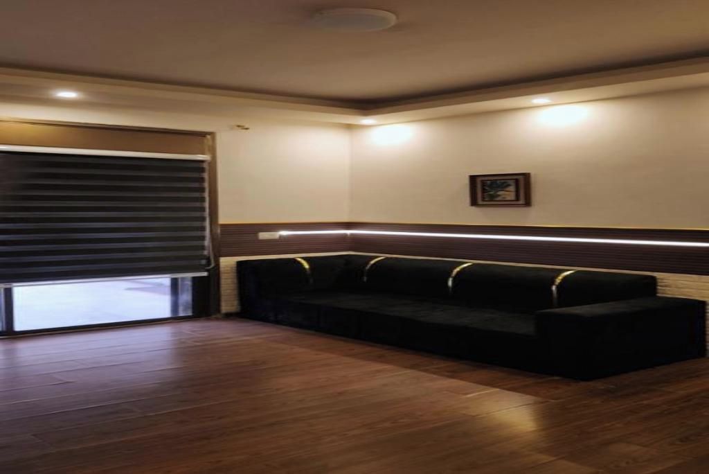 Una habitación con un sofá de color oscuro, suelo de madera, una lámpara en el techo y un cuadro enmarcado en la pared.