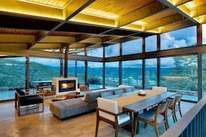 A modern interior with a fireplace, seating area, and large windows offering a view of the outdoors. - Exclusiva Casa en El Santuario, Vista al Lago (Valle de Bravo)
