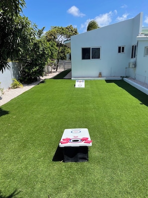 A backyard with artificial grass, a dartboard, and a small white building. - Luxury 4BR Villa • Pool • Walk to Palm Beach (Noord)