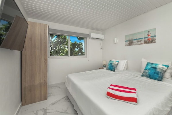 A bedroom with a bed, a window, an air conditioning unit, and a painting on the wall. - Luxury 4BR Villa • Pool • Walk to Palm Beach (Noord)