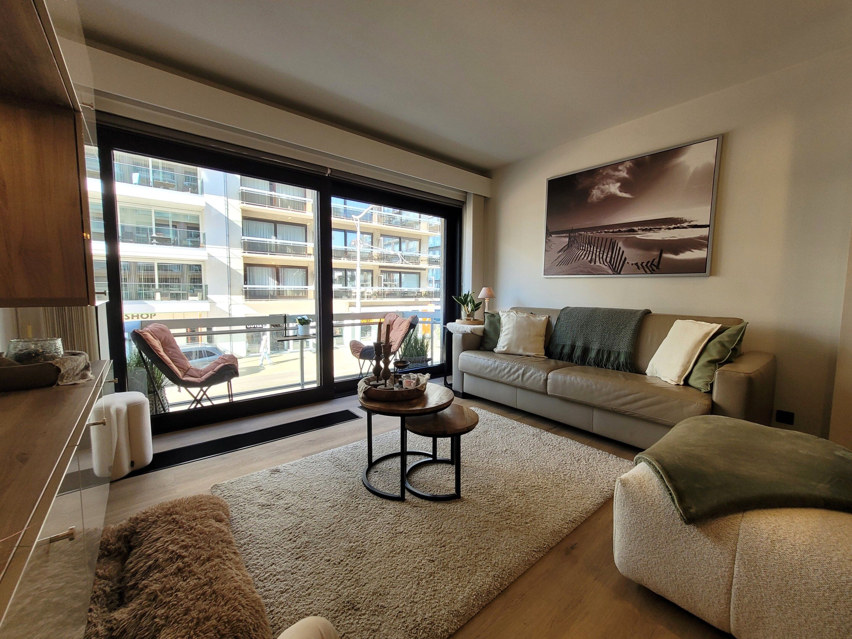 Un salon moderne avec un canapé, une table basse et une vue sur un immeuble à travers de grandes fenêtres.