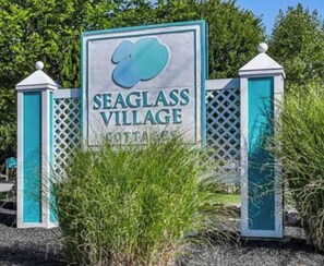 A sign for Seaglass Village with a logo, surrounded by greenery.