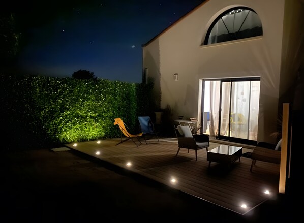 An outdoor patio with a wooden deck, seating area, and a green hedge. - Studio Apartment 'Gîte La Petite Chaunière' with Private Terrace, Wi-Fi and Air Conditioning (Saint-Fulgent)