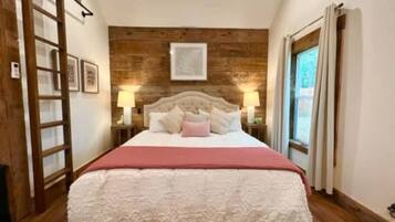 A bedroom with a bed, wooden wall paneling, a window with curtains, and a ladder.