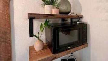 A kitchen with a microwave on a wooden shelf, a potted plant, and a vase.