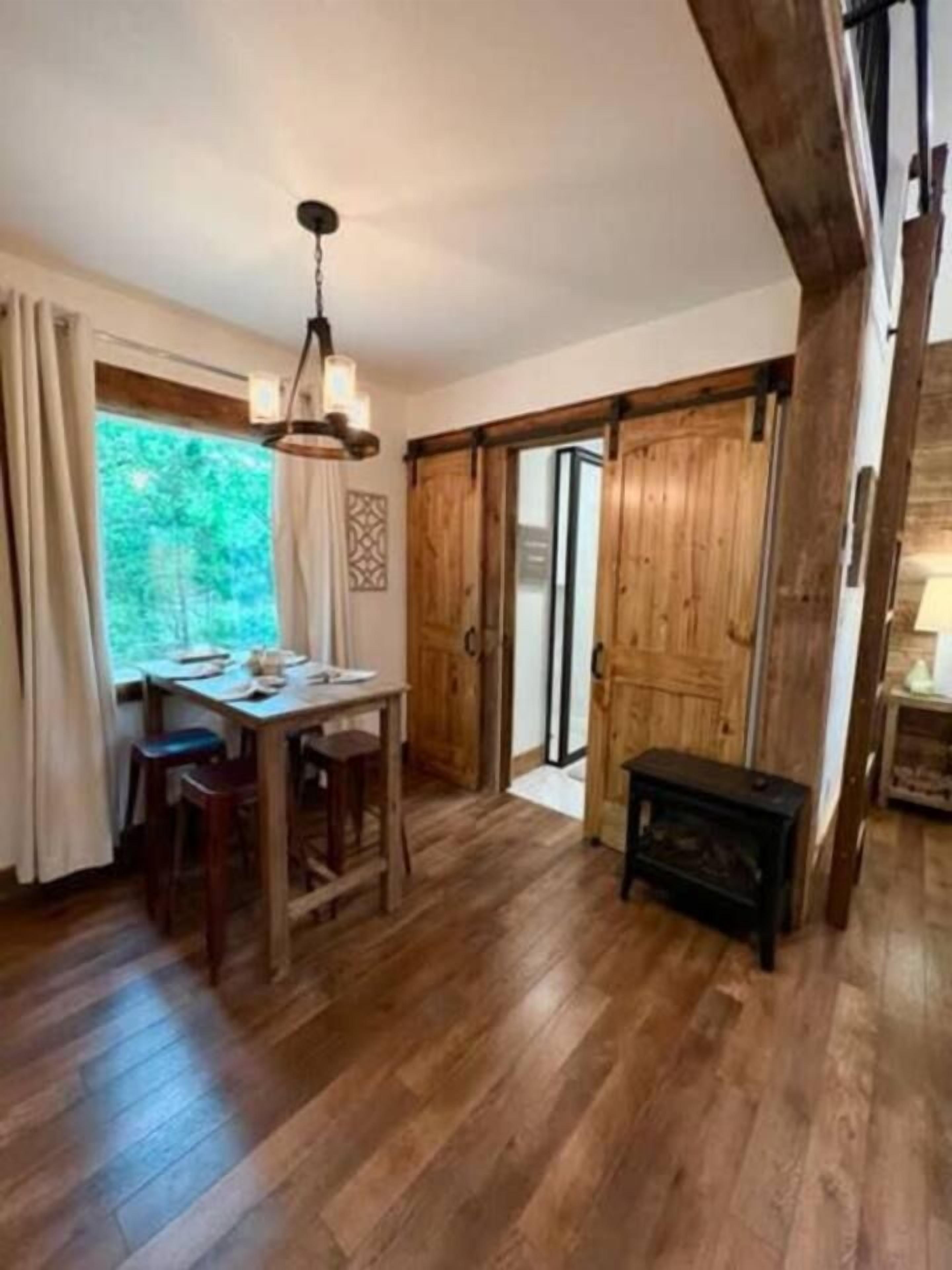 A wooden dining table with chairs, a hanging light fixture, and a sliding glass door leading outside.