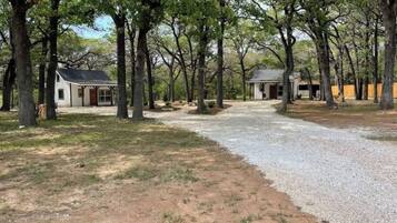 A residential area with two houses, a gravel driveway, and a wooded area.