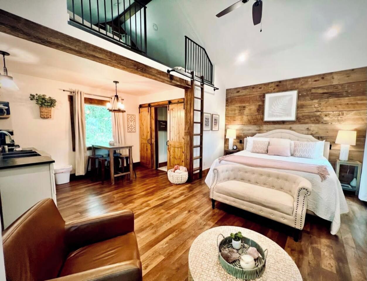 A spacious room with a loft area, a bed with a headboard, a dining table, and a kitchen area.