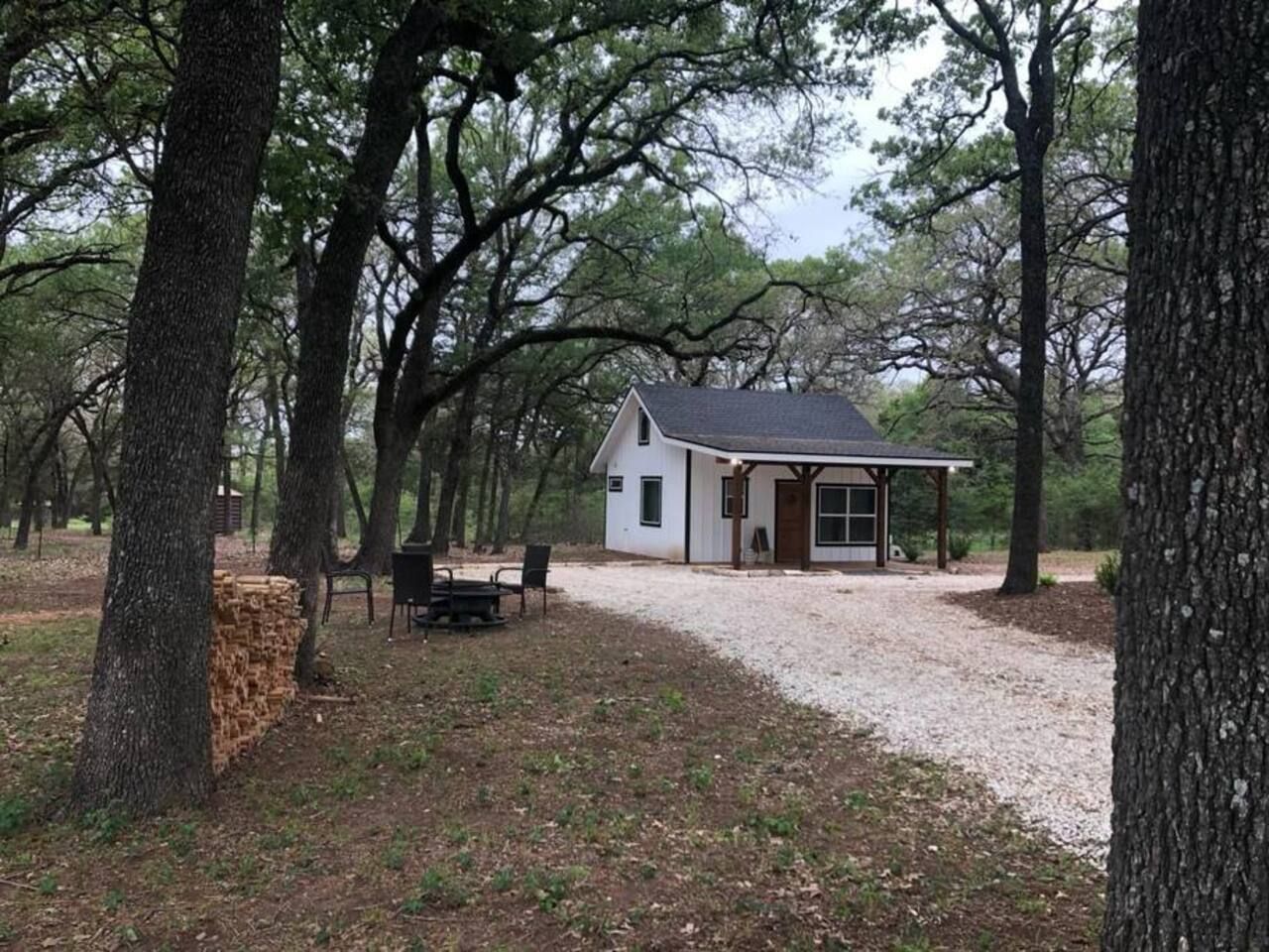 A small, single-story cabin with a porch, surrounded by trees.