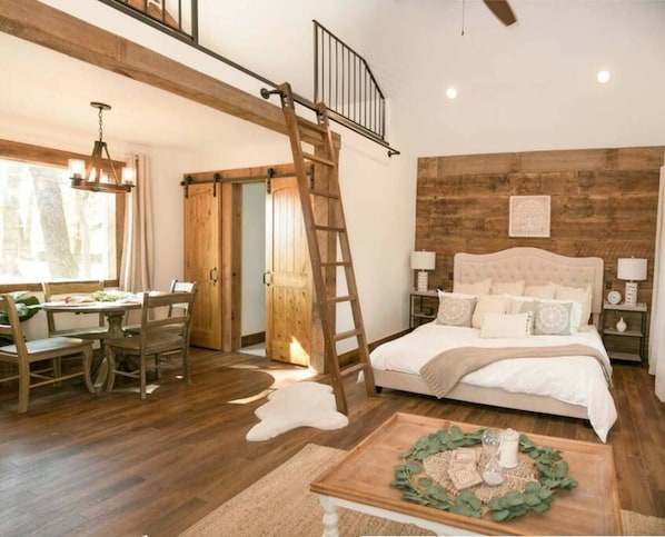 A bedroom with a bed, a wooden ladder, a dining table with chairs, and a view of the outdoors. - Plush Cabin 4 min to Homestead Heritage 18 min to (Waco)
