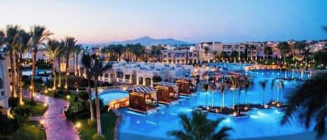 A resort with multiple swimming pools, palm trees, and a paved walkway.