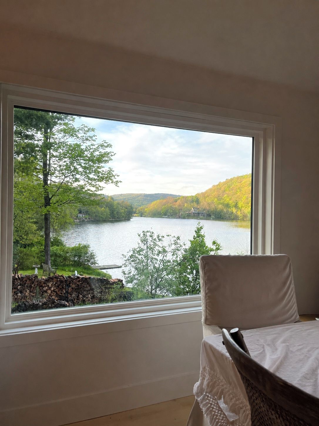 A bedroom with a large window offering a view of a lake and hills.