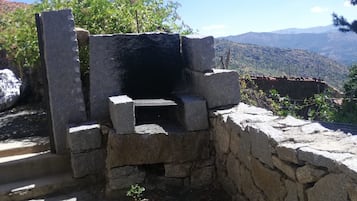 Une structure en pierre avec un banc, entourée de végétation et se dressant sur un fond de montagnes.
