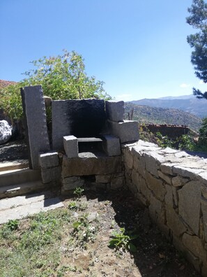 Una estructura de piedra con un banco, rodeada de vegetación y un paisaje montañoso.