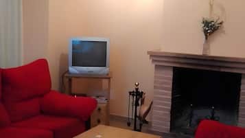 Un salon avec une cheminée, un téléviseur posé sur un meuble et deux canapés rouges.