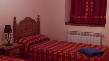 Une chambre avec deux lits, une table de chevet, une lampe, une fenêtre avec des rideaux et un radiateur.