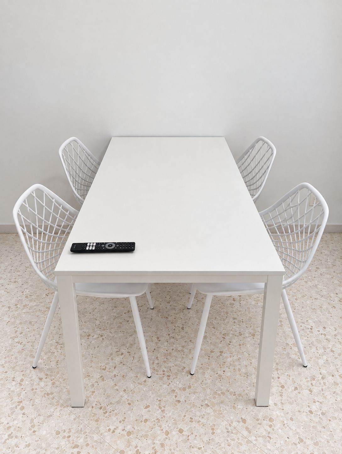 Een witte tafel met vier witte stoelen, een afstandsbediening op de tafel en een stippelde vloer.