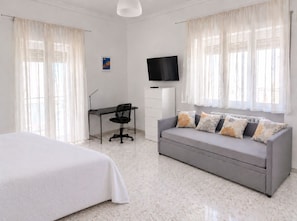 Ein Hotelzimmer mit Bett, Schreibtisch, Stuhl, Sofa, Fernseher und einem Fenster mit Vorhängen.