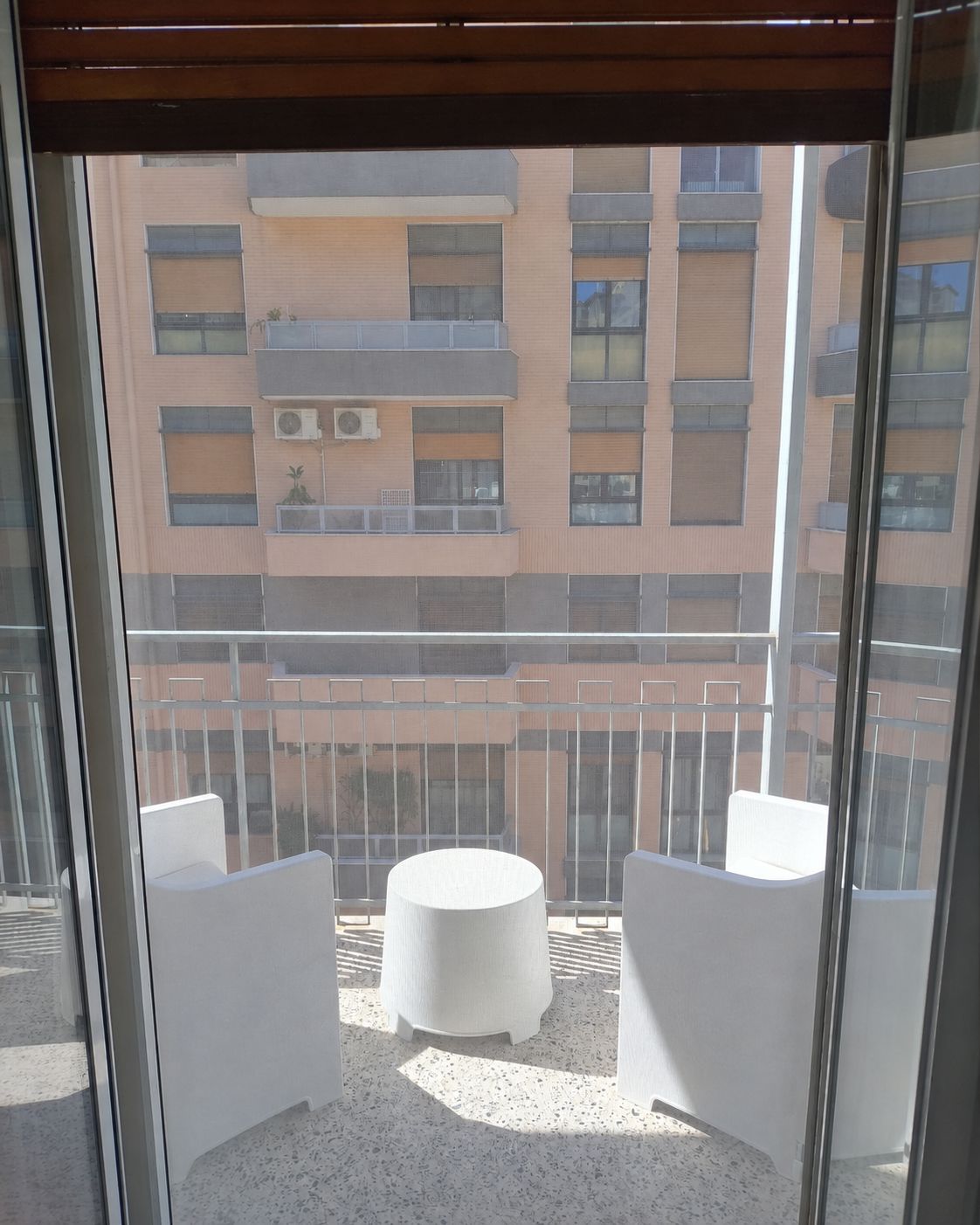 Een balkon met twee witte stoelen en een kleine ronde tafel, met uitzicht op een gebouw met meerdere balkons.
